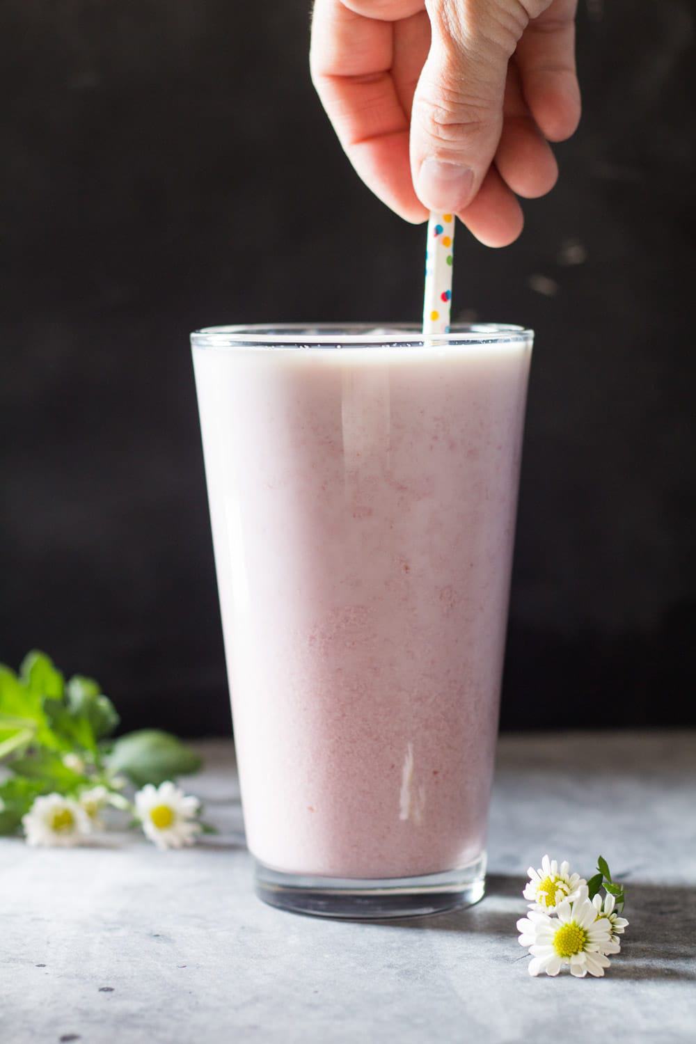 Hand holding a straw in a tall glass of Raspberry Milk.