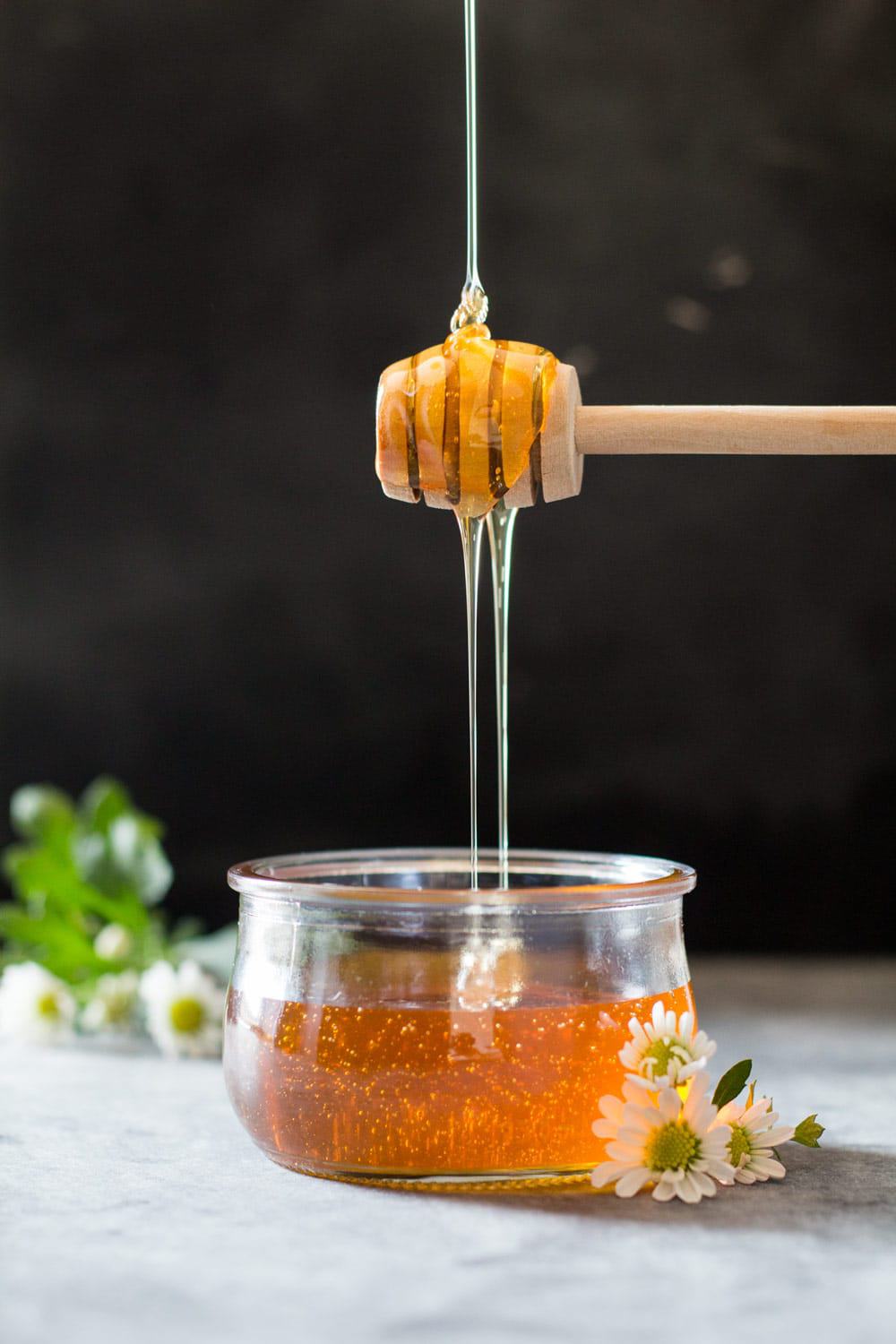 Honey pouring from a honey stick into a glass jar of honey.