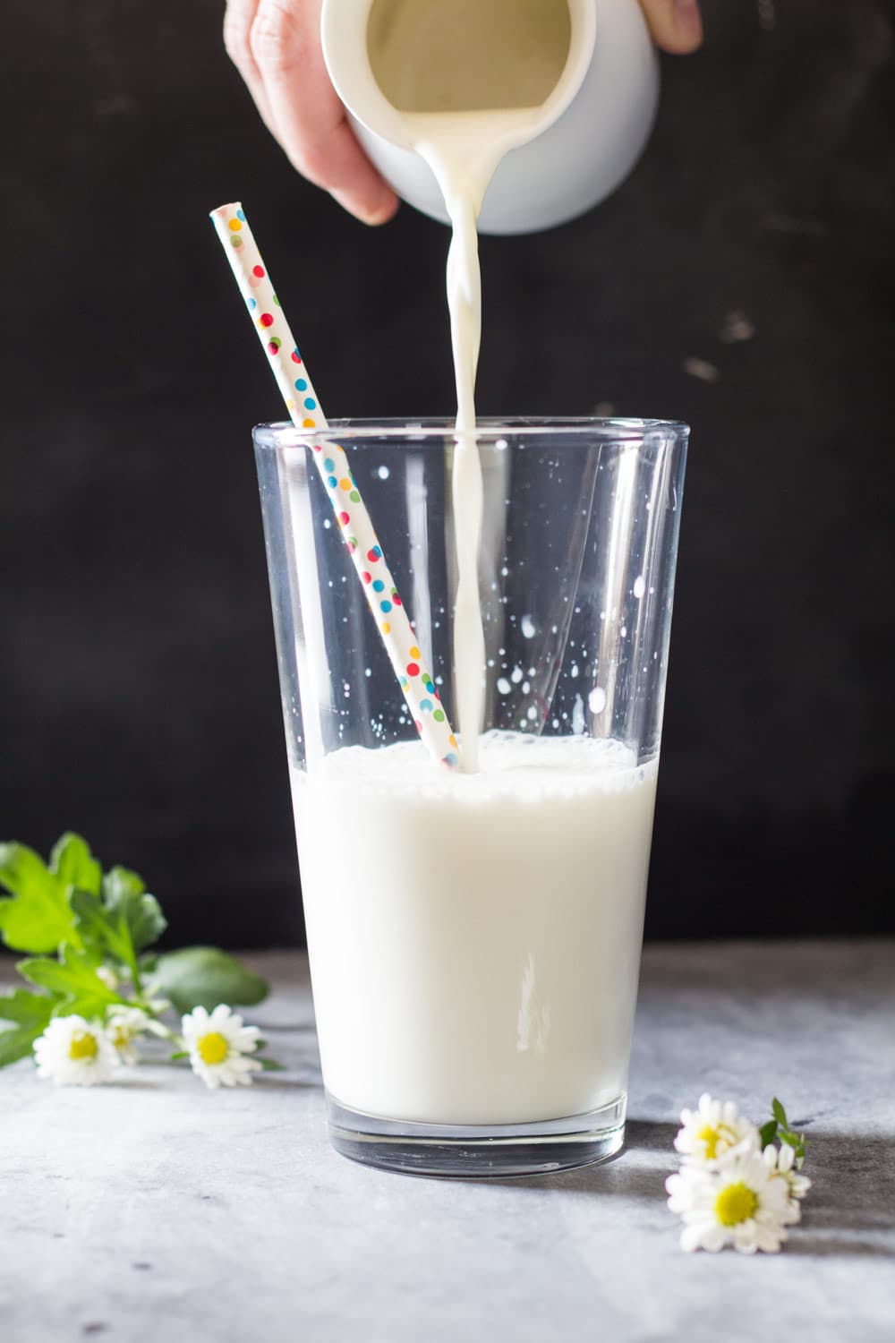 Milk being poured in a tall glass with a confetti straw from a white milk jar.