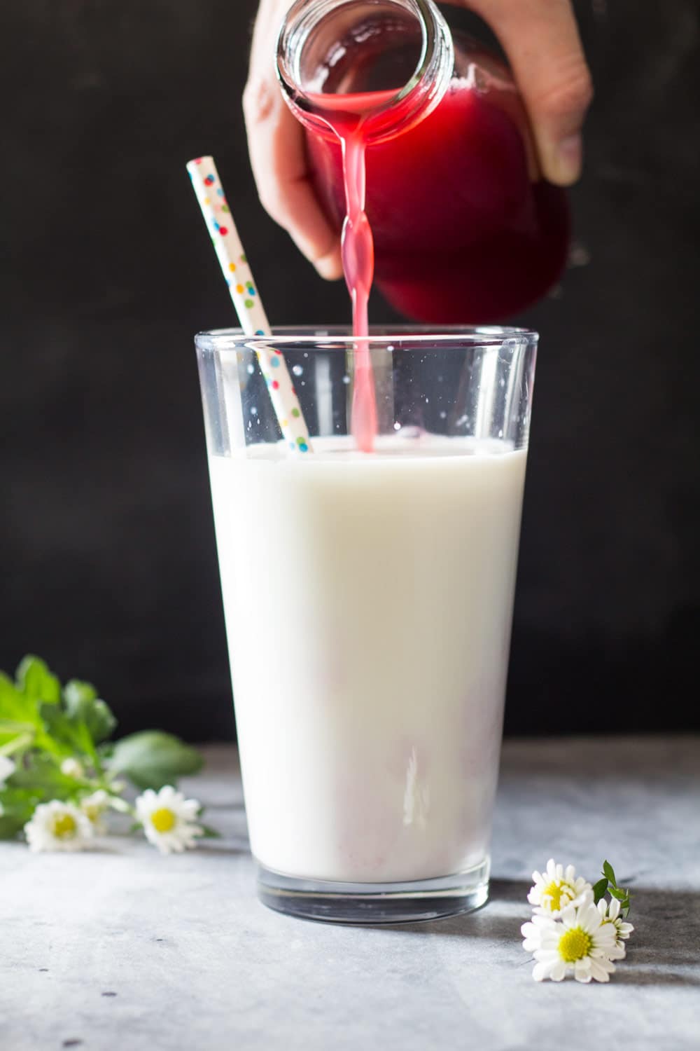 Raspberry juice being poured into a tall glass of milk with a confetti straw.
