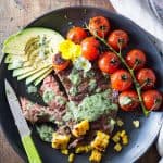 Skirt Steak with Basil Cream and Grilled Tomatoes, corn kernels and sliced avocado, a knife, and a jar of Basil Cream.