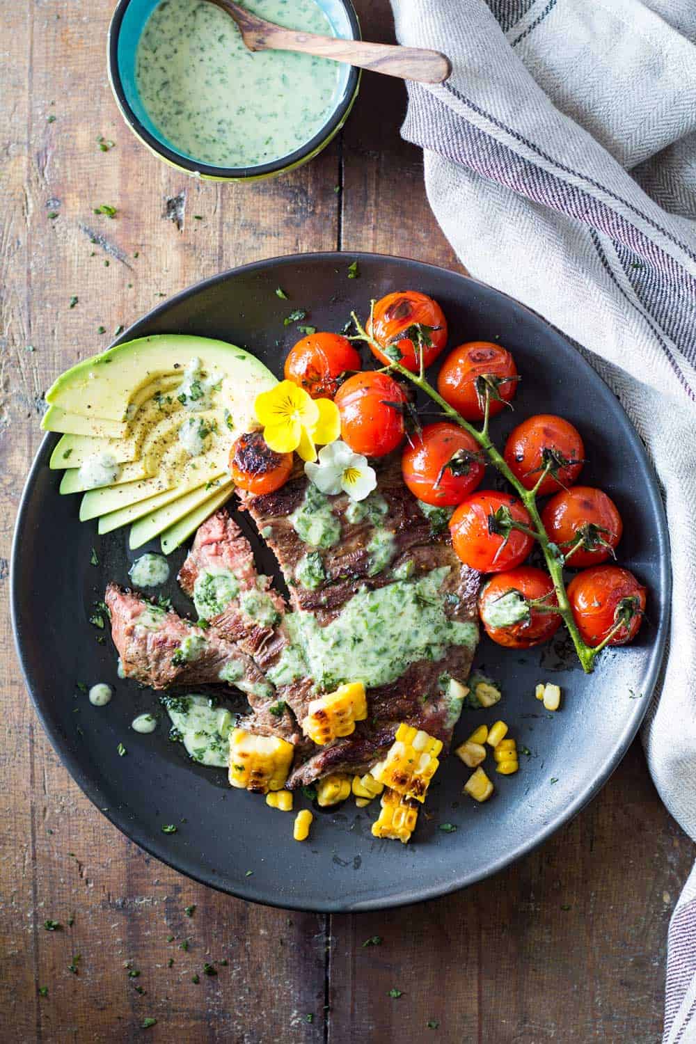 Skirt Steak with Basil Cream and Grilled Tomatoes, corn kernels and sliced avocado, and a jar of Basil Cream with a wooden spoon.