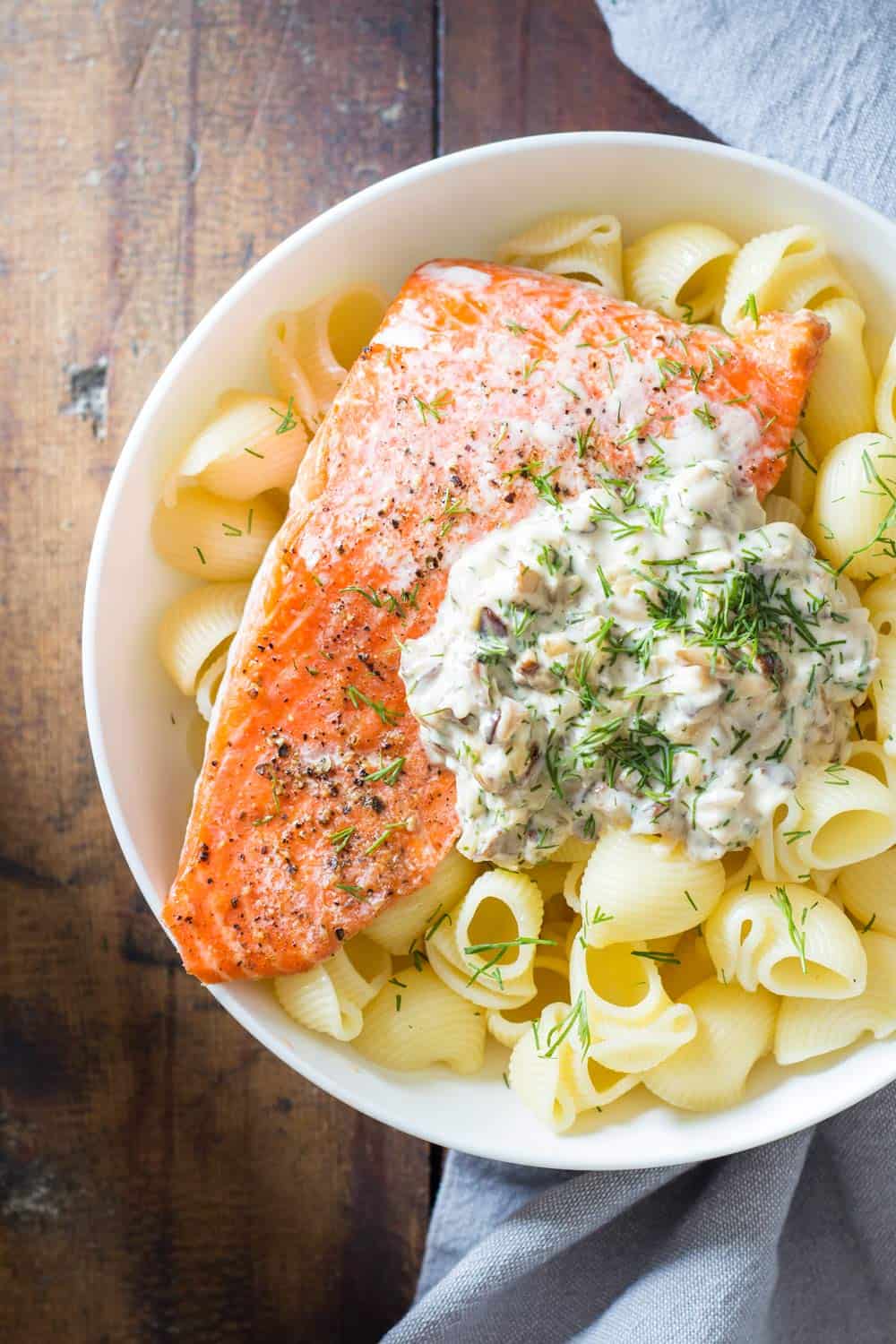 Top view of Sockeye Salmon Pasta with Shiitake mushroom sauce and fresh dill in a white bowl, and a napkin beside it.