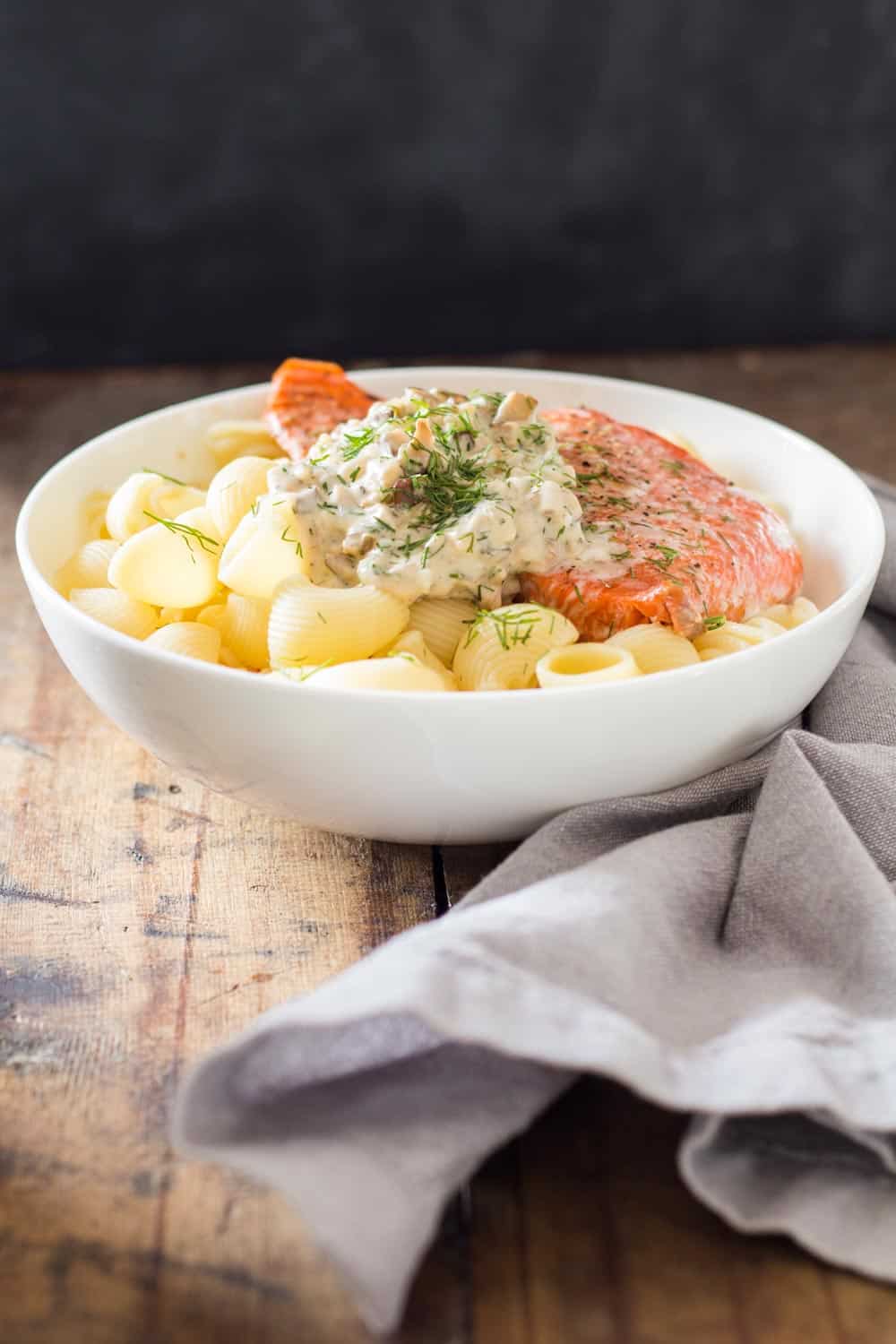 Sockeye Salmon Pasta with Shiitake mushroom sauce and fresh dill in a white bowl, and a napkin beside it.