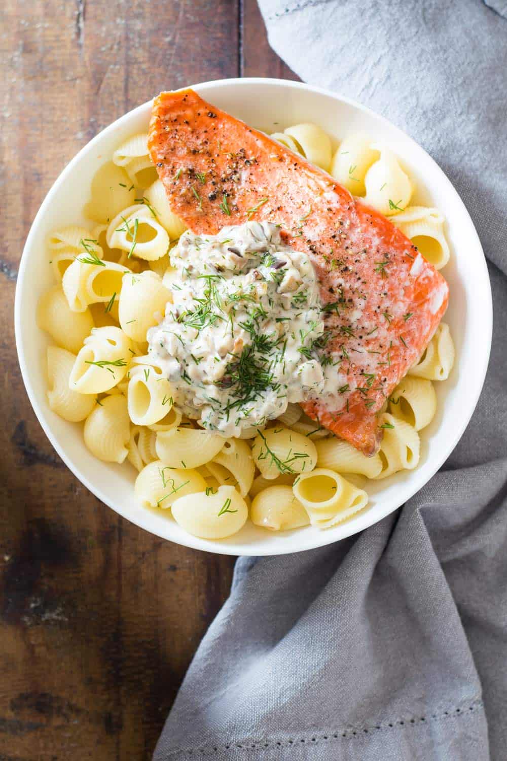 Top view of Sockeye Salmon Pasta with Shiitake mushroom sauce and fresh dill in a white bowl, and a napkin beside it.