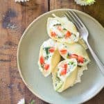 Spinach Ricotta Stuffed Shells on a plate with a fork, on a wooden table with flowers.