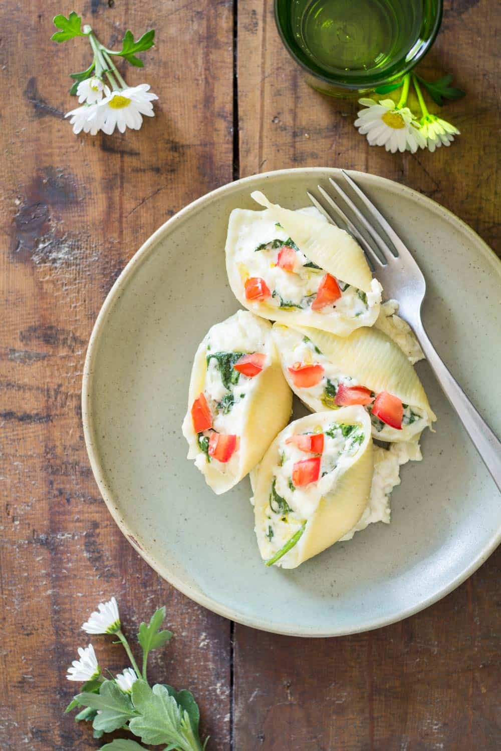 Spinach Ricotta Stuffed Shells on a plate with a fork, on a wooden table with flowers.