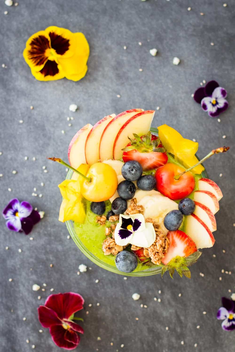 Top view of Green Smoothie Bowl decorated with fresh fruit and fresh flowers.