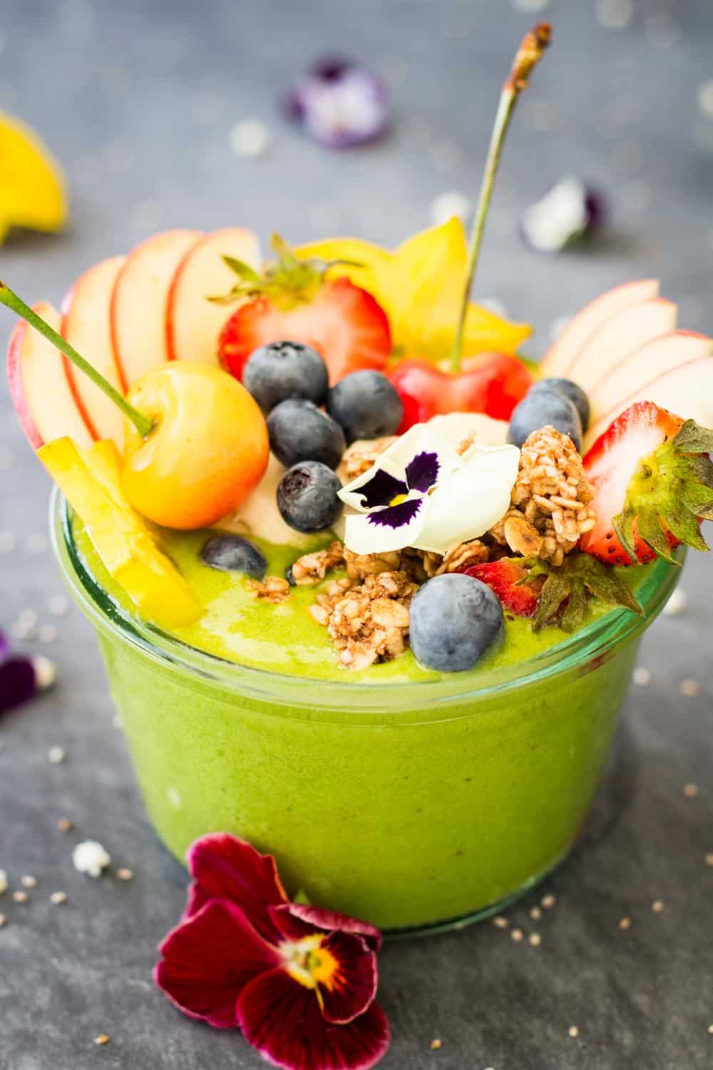 Close up of Green Smoothie Bowl topped with fresh fruit and fresh flowers.