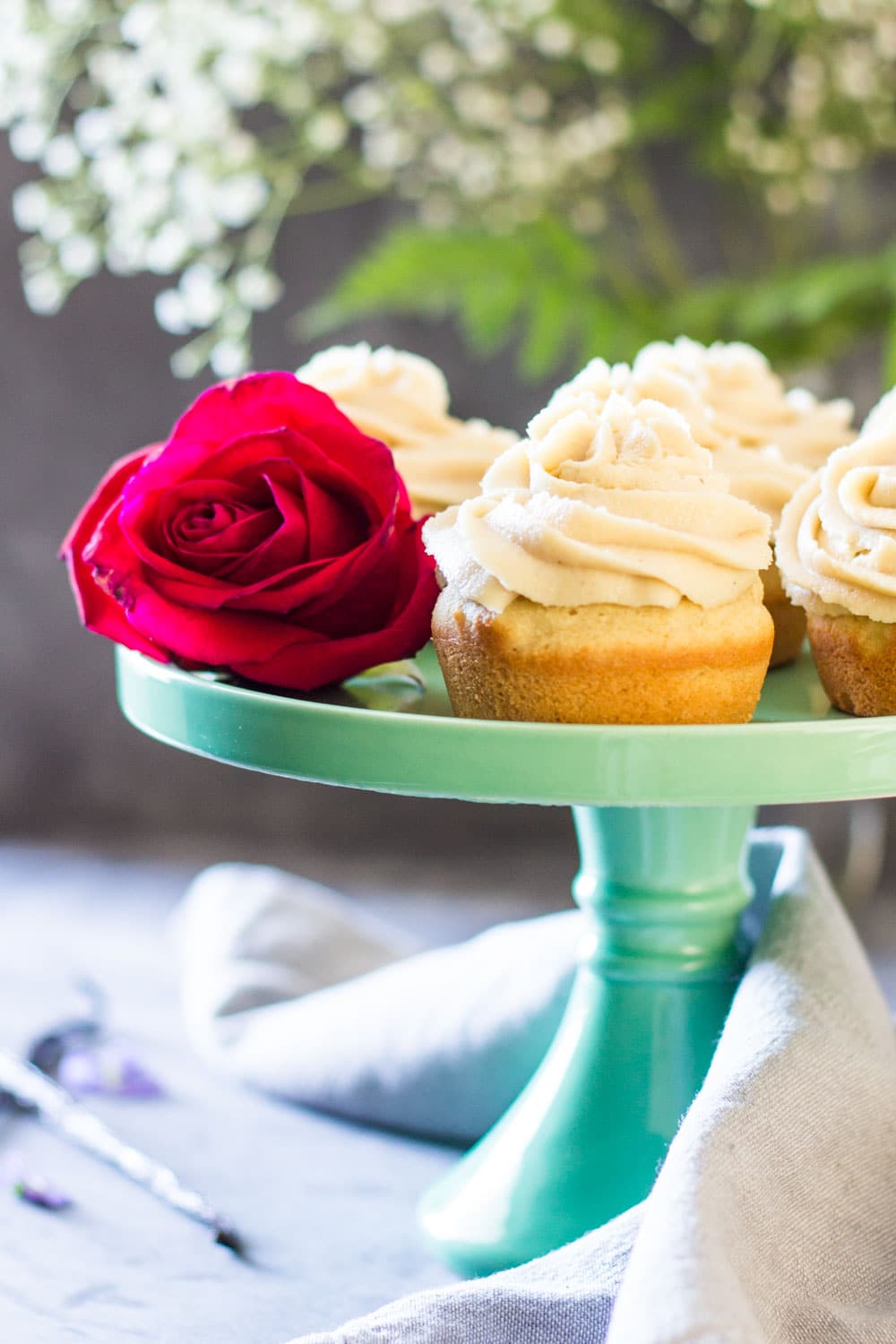 Moist Vanilla Cupcakes on a green cake stand with a rose.