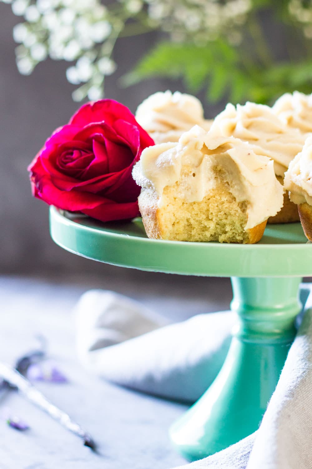 Bitten Moist Vanilla Cupcake on a green cake stand with a rose.