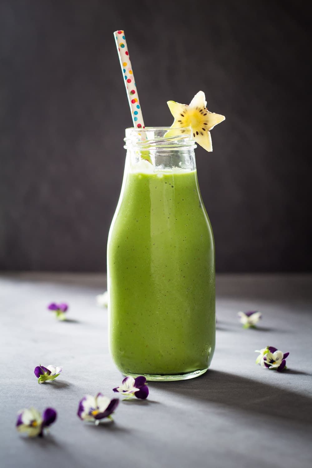 Green Smoothie For Kids in a glass bottle with a confetti straw and a star-shaped kiwi slice.