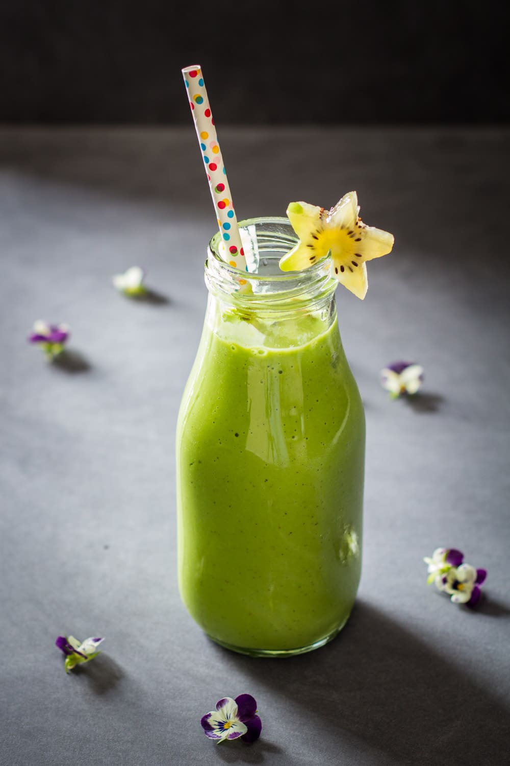 Green Smoothie For Kids in a glass bottle with a confetti straw and a star-shaped kiwi slice.