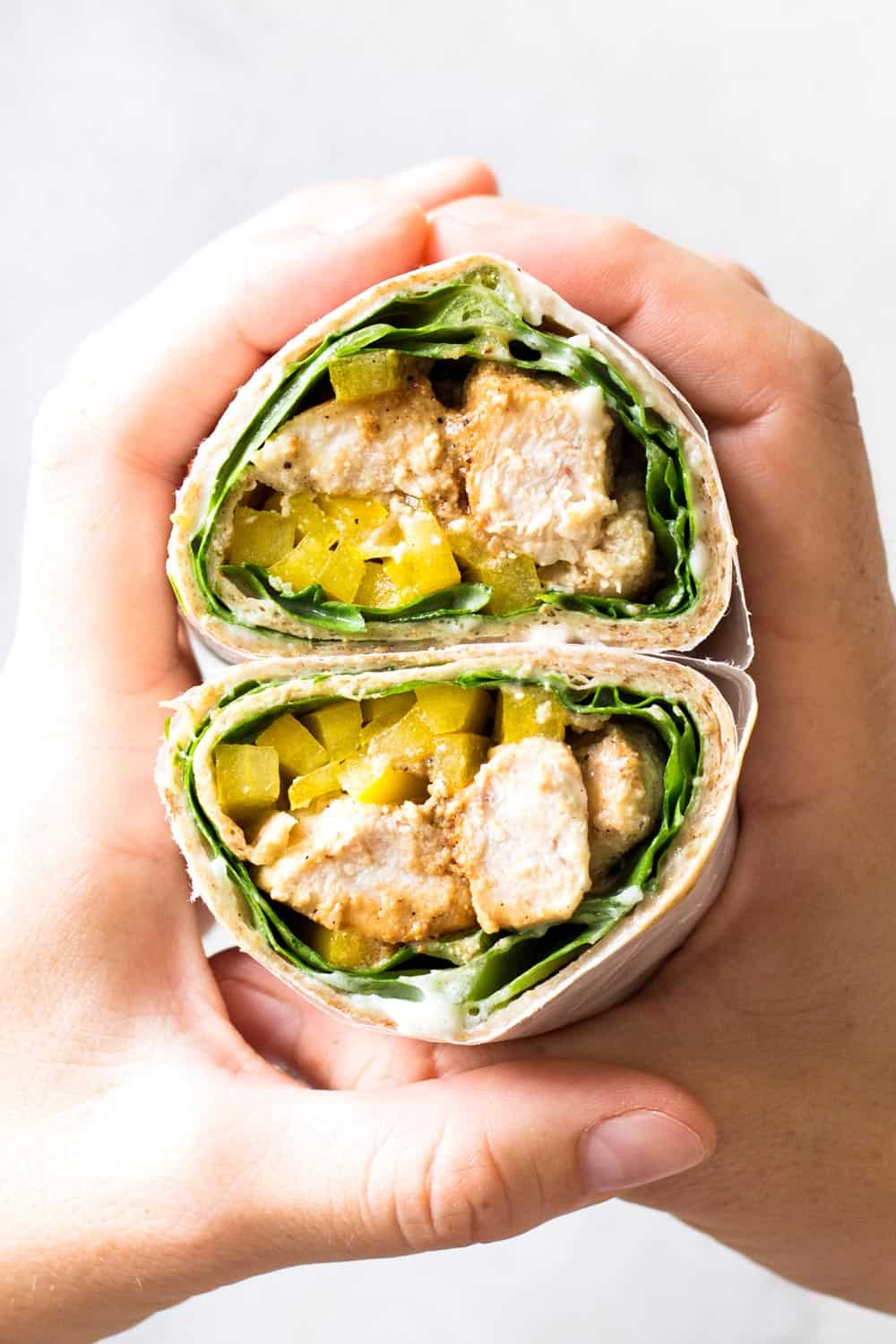 Hands holding two halves of a sliced Healthy Chicken Wrap.