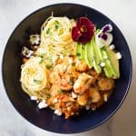 Top view of Mexican-Style Shrimp Capellini Pasta in a black bowl decorated with fresh flowers.