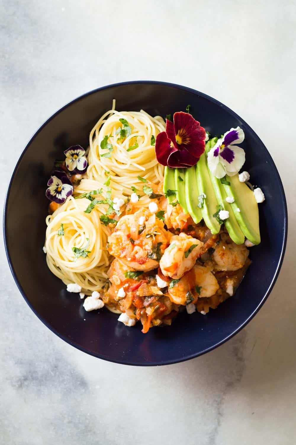 Top view of Mexican-Style Shrimp Capellini Pasta in a black bowl decorated with fresh flowers.