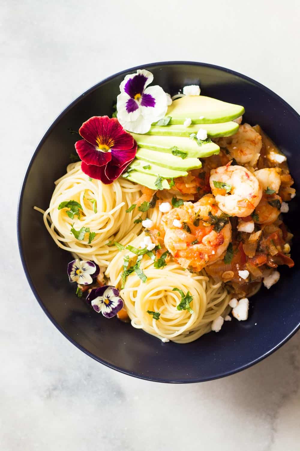 Top view of Mexican-Style Shrimp Capellini Pasta in a black bowl decorated with fresh flowers.