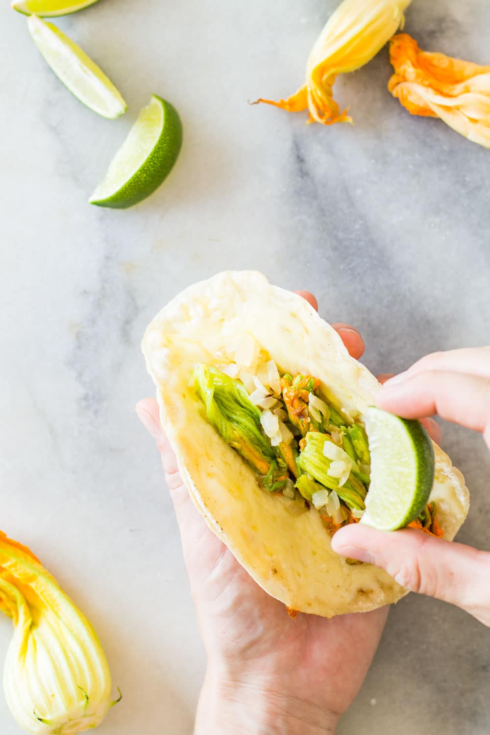 Hand holding a Squash Blossom Quesadilla and squeezing a lime on it.