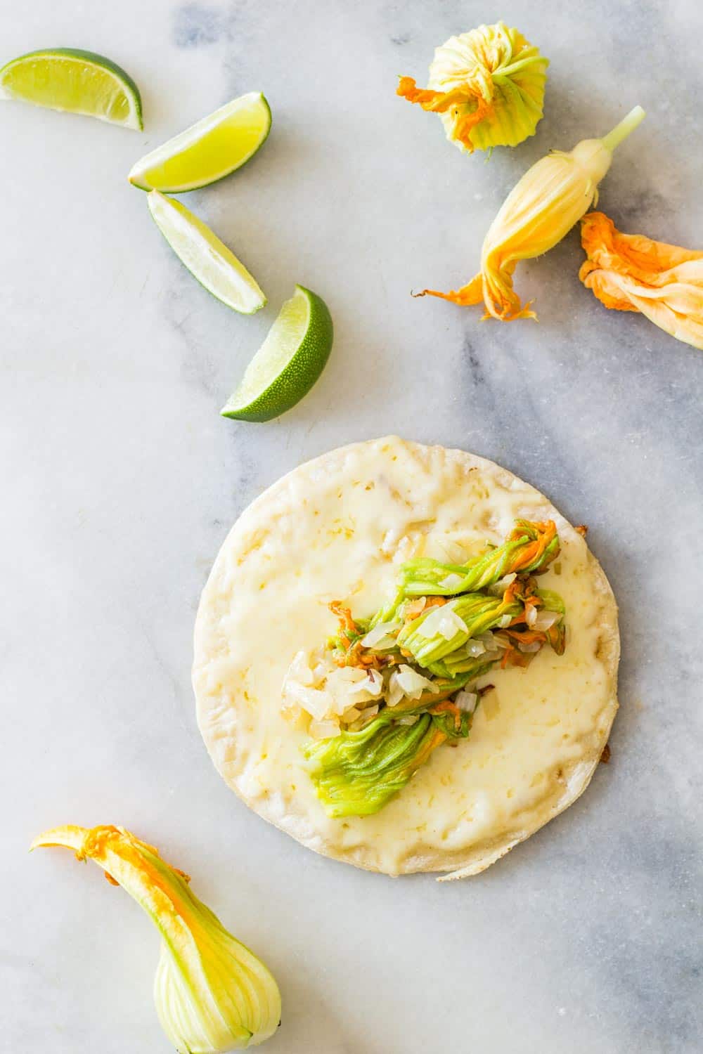 An open Squash Blossom Quesadilla, a sliced lime and squash blossoms on a marble surface.