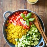 Turmeric Quinoa Salad in a blue bowl with wooden salad spoon and fork, and a jar of honey mustard dressing with a wooden spoon.