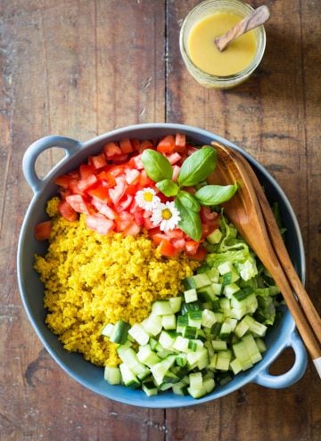 Turmeric Quinoa Salad in a blue bowl with wooden salad spoon and fork, and a jar of honey mustard dressing with a wooden spoon.