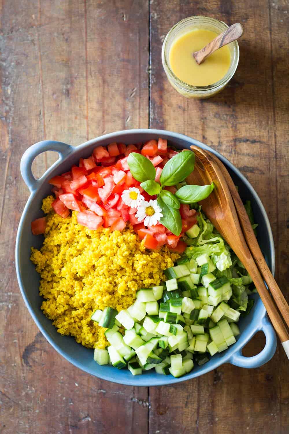 Turmeric Quinoa Salad in a blue bowl with wooden salad spoon and fork, and a jar of honey mustard dressing with a wooden spoon.