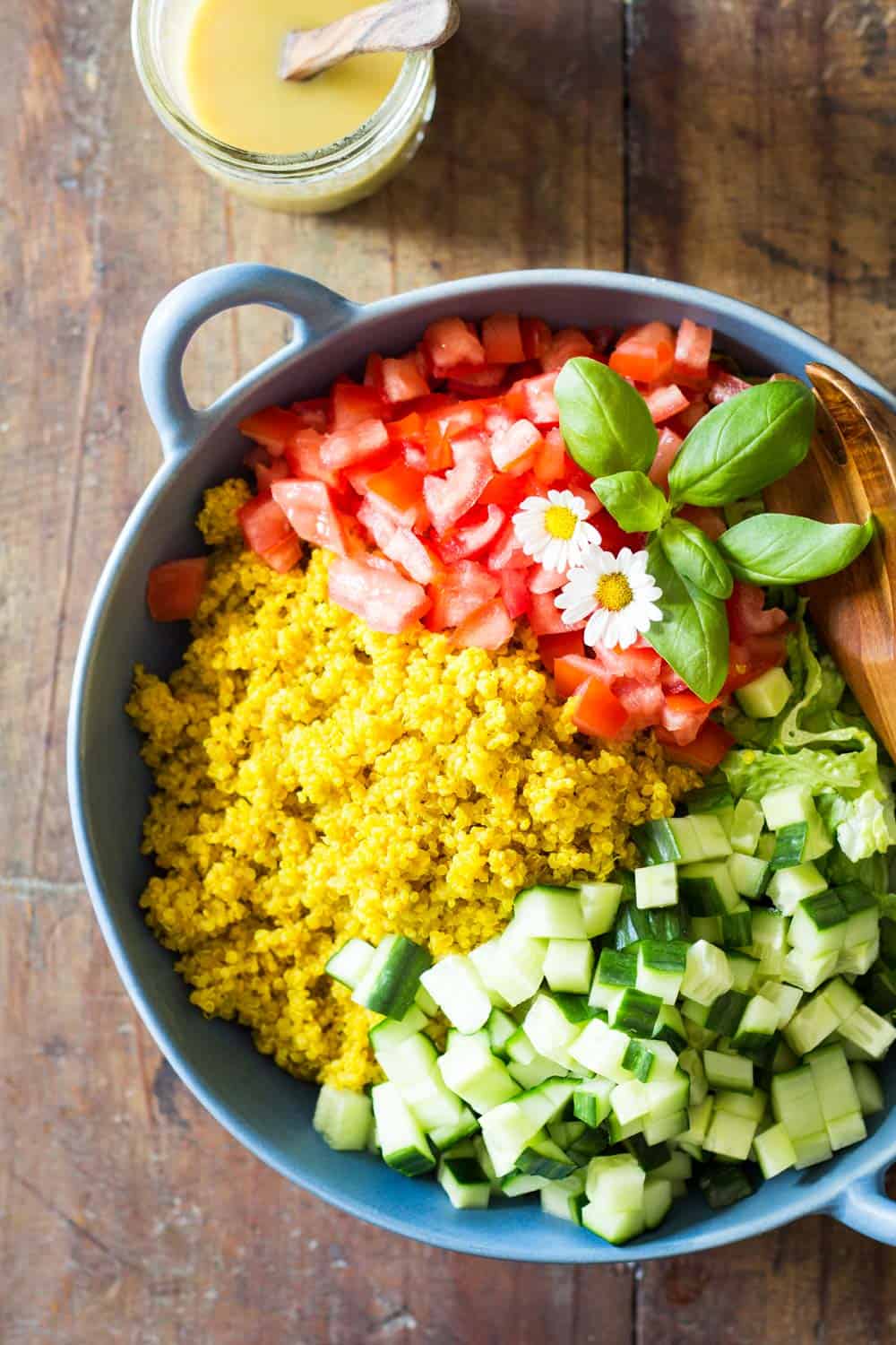 Turmeric Quinoa Salad in a blue bowl, and a jar of honey mustard dressing with a wooden spoon.