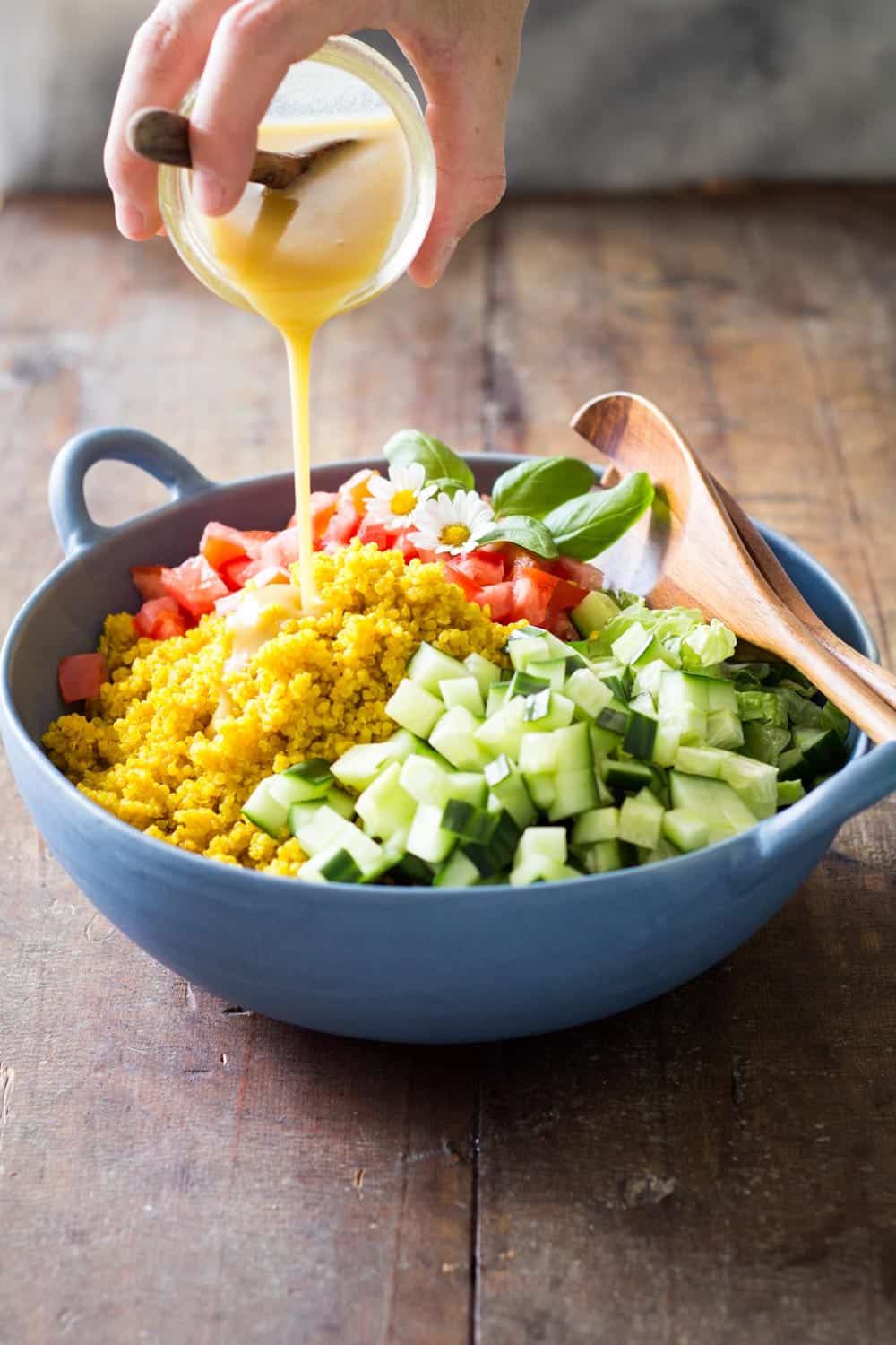 Honey mustard dressing being poured over a bowl of Turmeric Quinoa Salad and a wooden salad spoon.