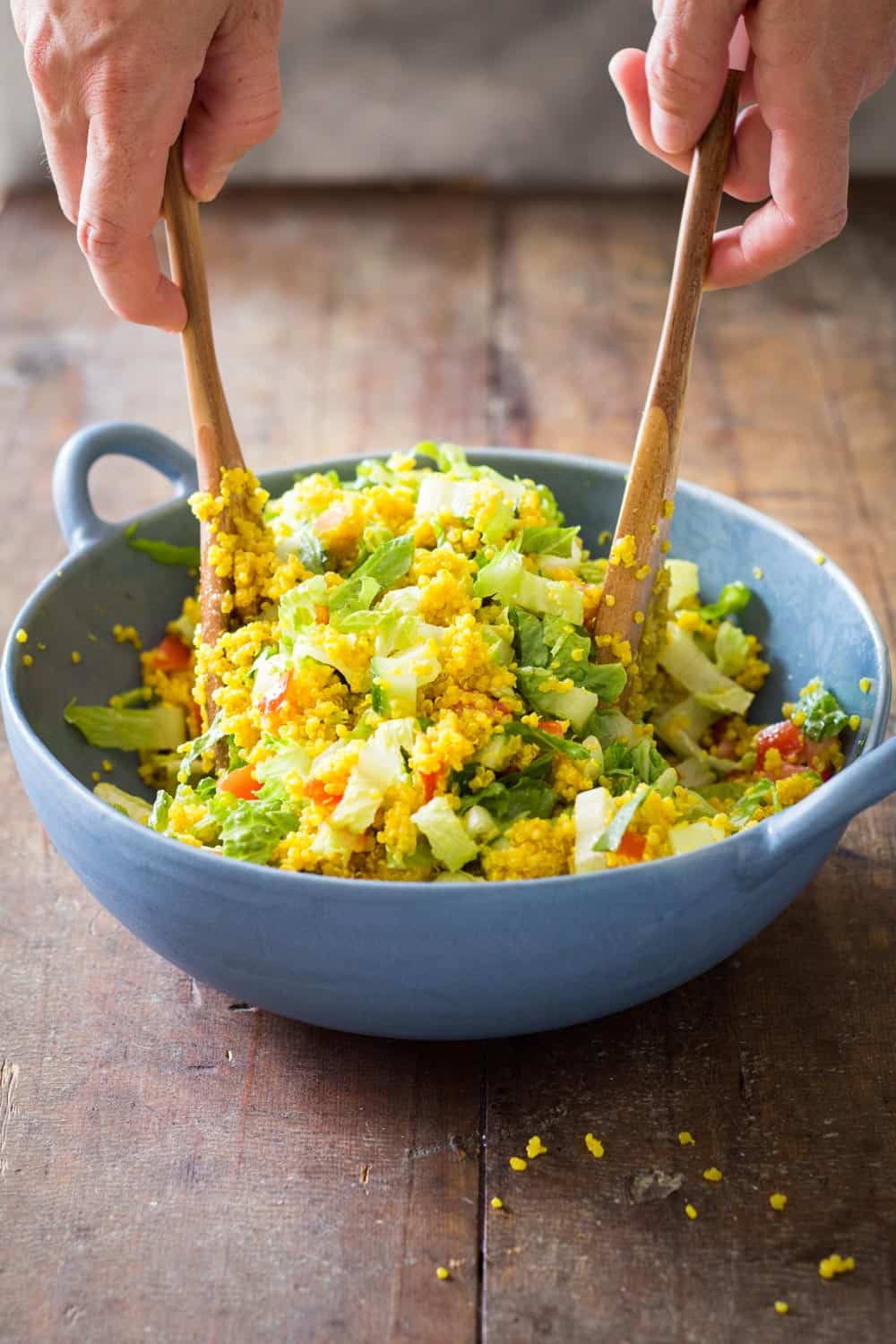 Hands mixing Turmeric Quinoa Salad with a wooden salad fork and spoon.