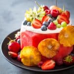 Vegan Watermelon Cake on a black plate decorated with fresh fruit.