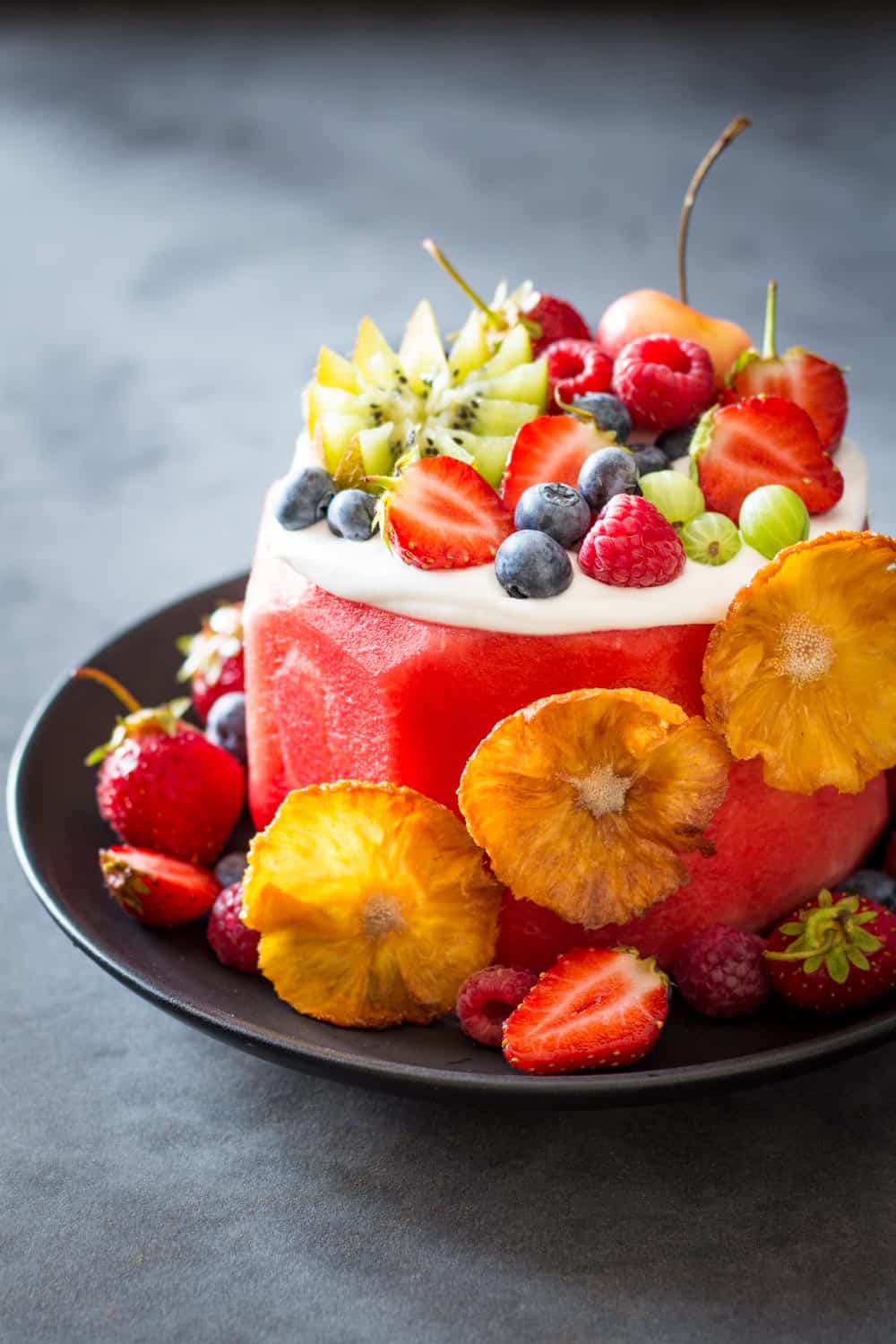 Vegan Watermelon Cake on a black plate decorated with fresh fruit.