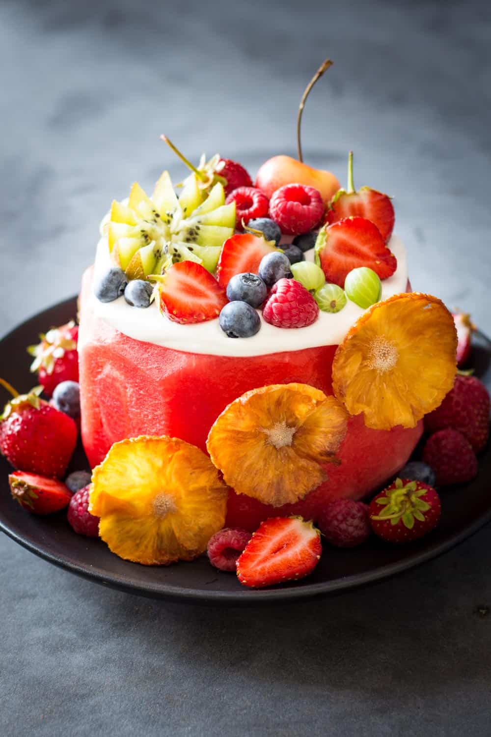 Vegan Watermelon Cake on a black plate decorated with fresh fruit.