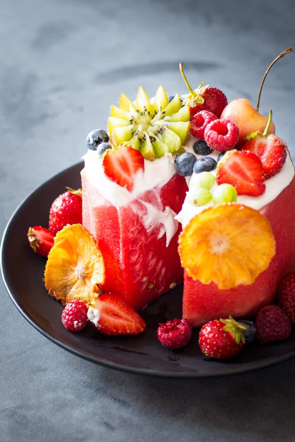 Sliced Vegan Watermelon Cake on a black plate decorated with fresh fruit.