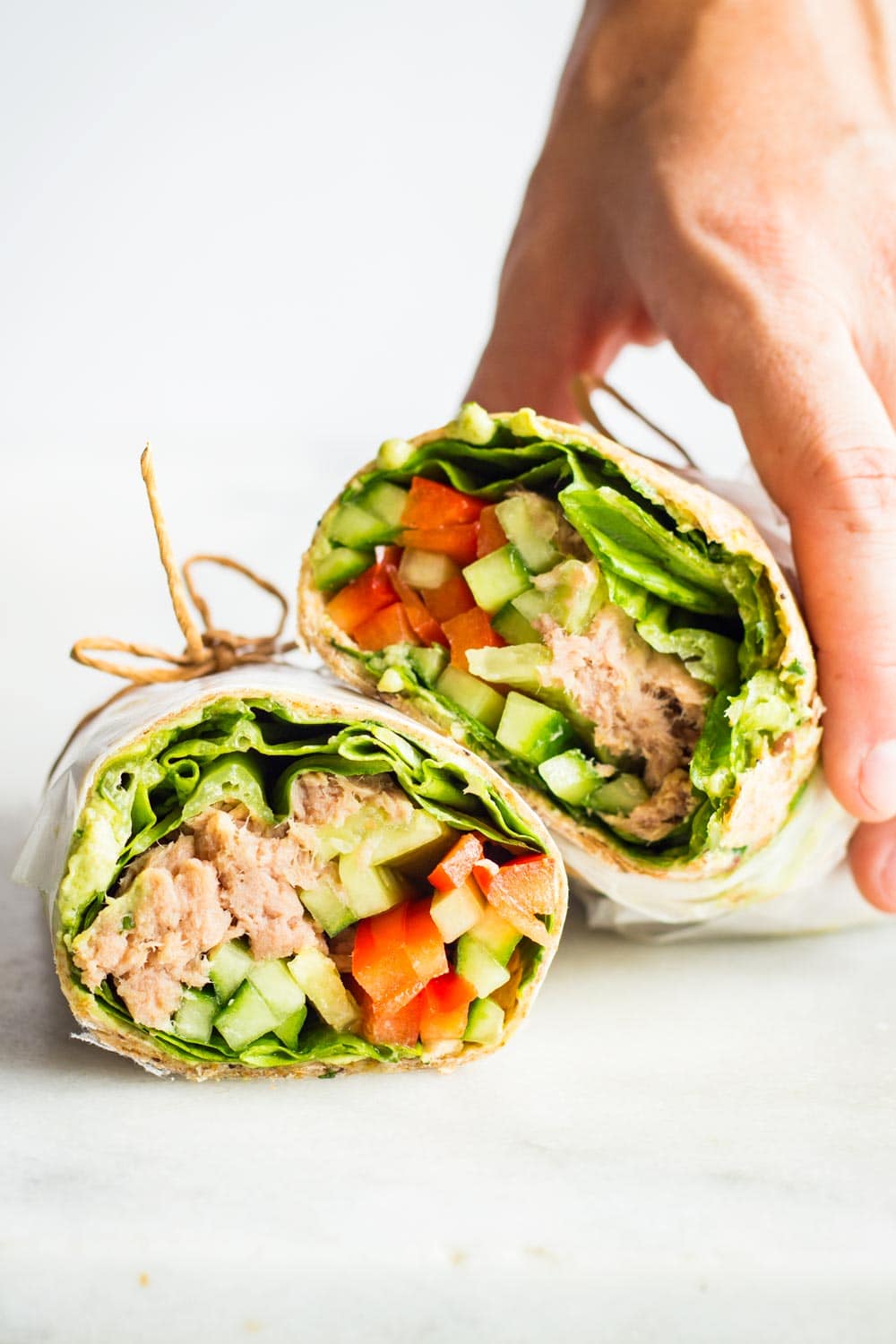 Hand holding a Healthy Tuna Wrap cut in two halves tied with jute twine.