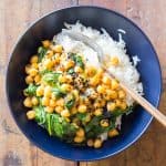 Top view of Chickpea Spinach Curry in a blue bowl with a fork, on a rustic wood table.