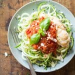 Top view of Easy Chicken Zoodles topped with tomato sauce, garnished with fresh basil leaves, and a fork.