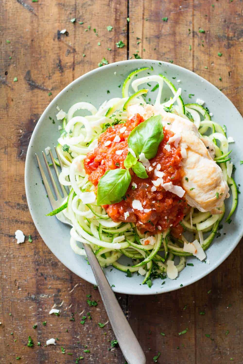 Top view of Easy Chicken Zoodles topped with tomato sauce, garnished with fresh basil leaves, and a fork.