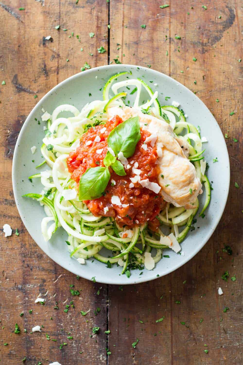 Top view of Easy Chicken Zoodles topped with tomato sauce, garnished with fresh basil leaves.