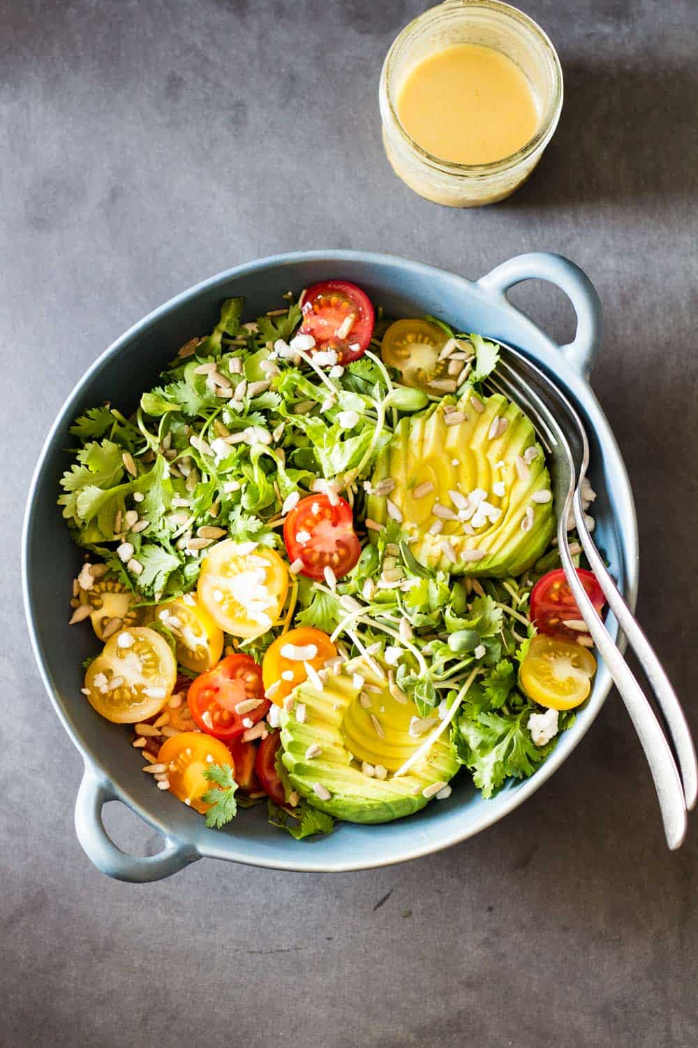 Top view of Mexican-Style Side Salad in a blue ceramic bowl with a fork and a spoon, and a jar of honey lime dressing.