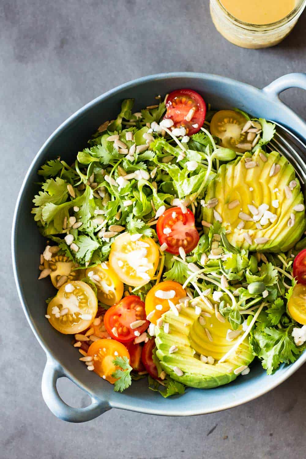 Top view of Mexican-Style Side Salad in a blue ceramic bowl, and a jar of honey lime dressing.