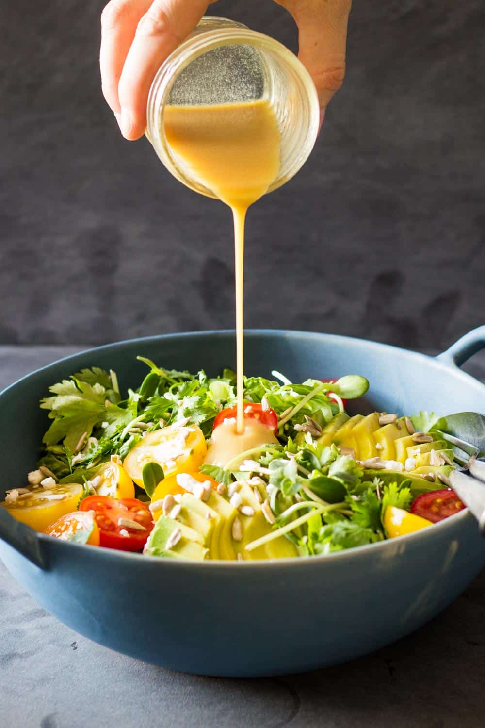 Honey lime dressing being poured over Mexican-Style Side Salad in a blue bowl.