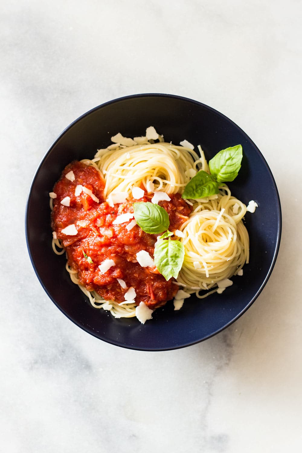 Capellini pasta topped with Roasted Garlic Tomato Sauce, garnished with fresh basil leaves, in a black bowl.