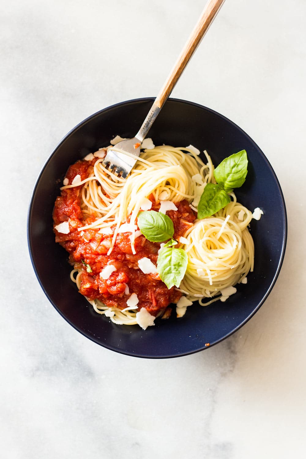 Capellini pasta topped with Roasted Garlic Tomato Sauce, garnished with fresh basil leaves, in a black bowl with a fork.
