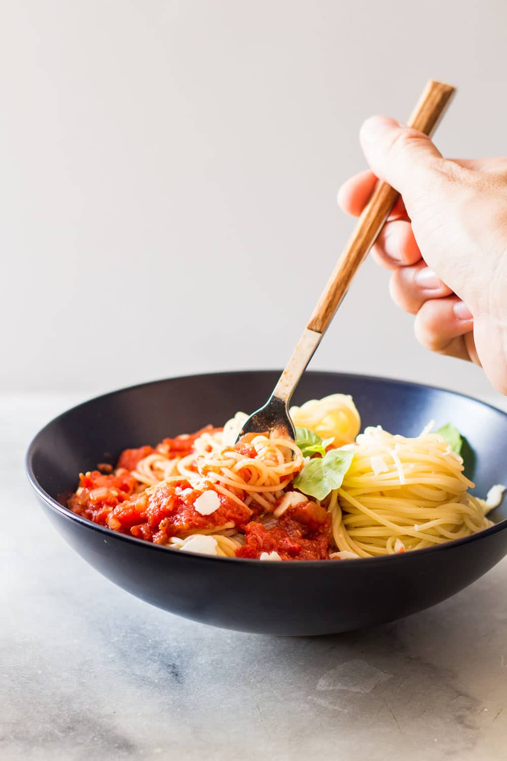 Hand grabbing some Capellini pasta with Roasted Garlic Tomato Sauce with a fork.