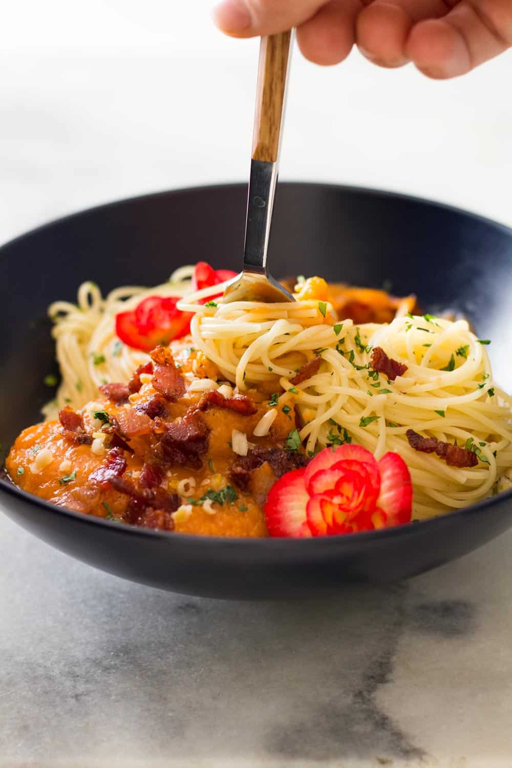 Hand grabbing spaghetti with a fork from a Butternut Squash Pasta with Bacon bowl.