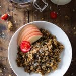 Bowl of Healthy Pumpkin Granola with apple slices, a jar with pumpkin granola, and part of a milk bottle.