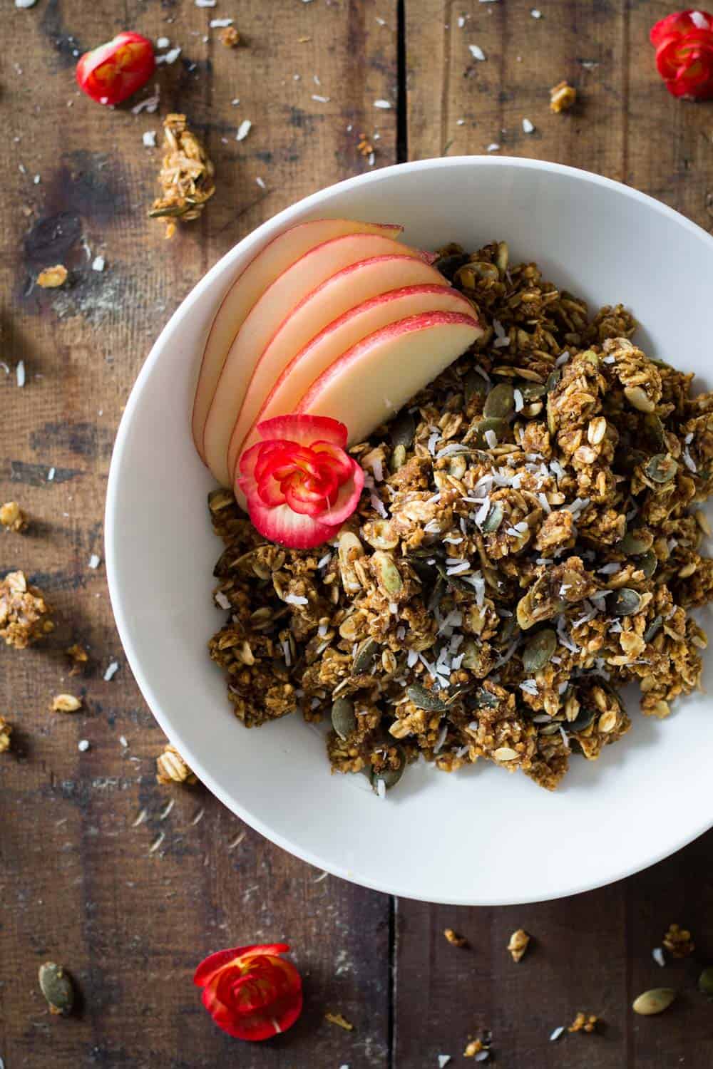 Healthy Pumpkin Granola in a white bowl with sliced apple.