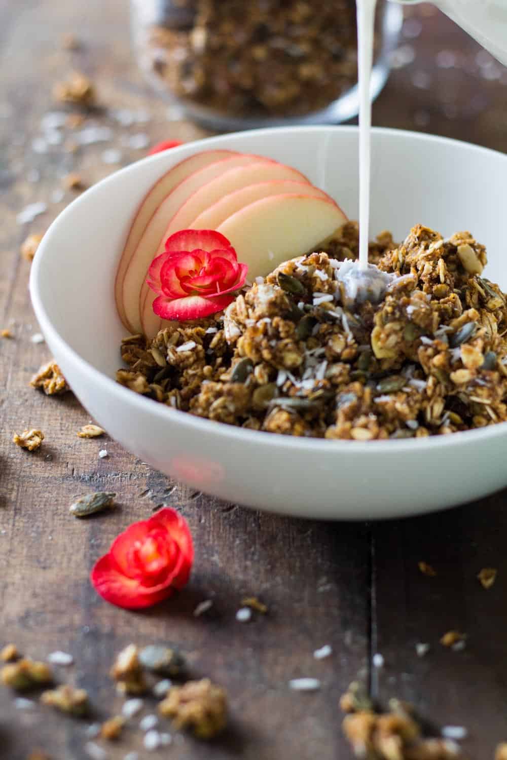 Milk being poured over bowl of Healthy Pumpkin Granola with apple slices.