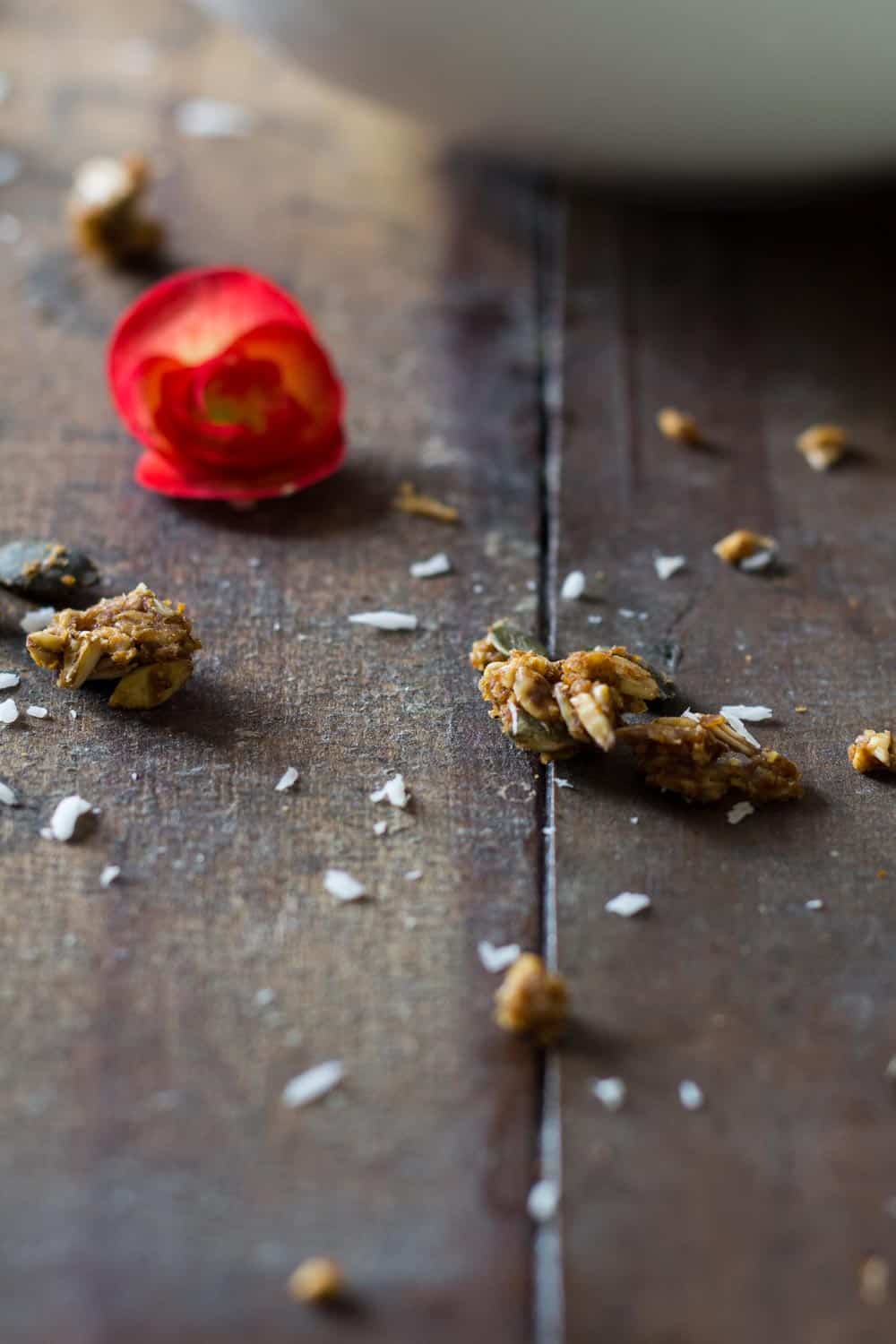 Close up of a piece of Healthy Pumpkin Granola on a rustic wooden table an a fresh flower.