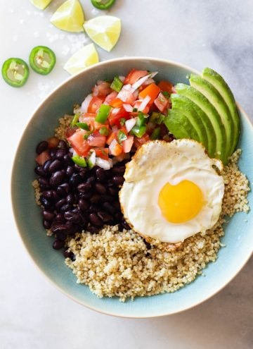 quinoa, black beans, fried egg, pico de gallo, sliced avocado in a blue bowl.